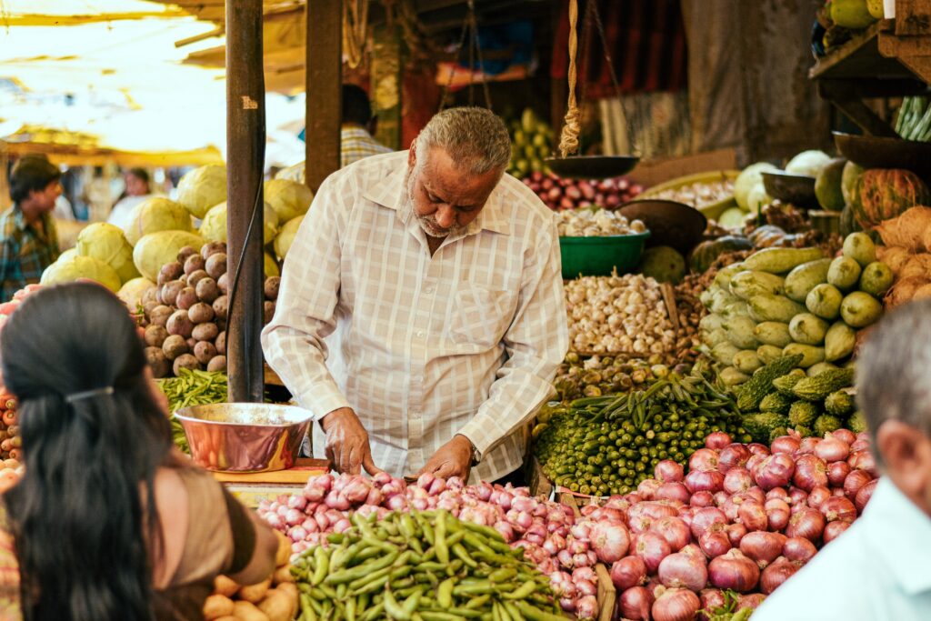 "Vendor at a local market displaying a fresh heap of onions, with customers browsing and making selections."